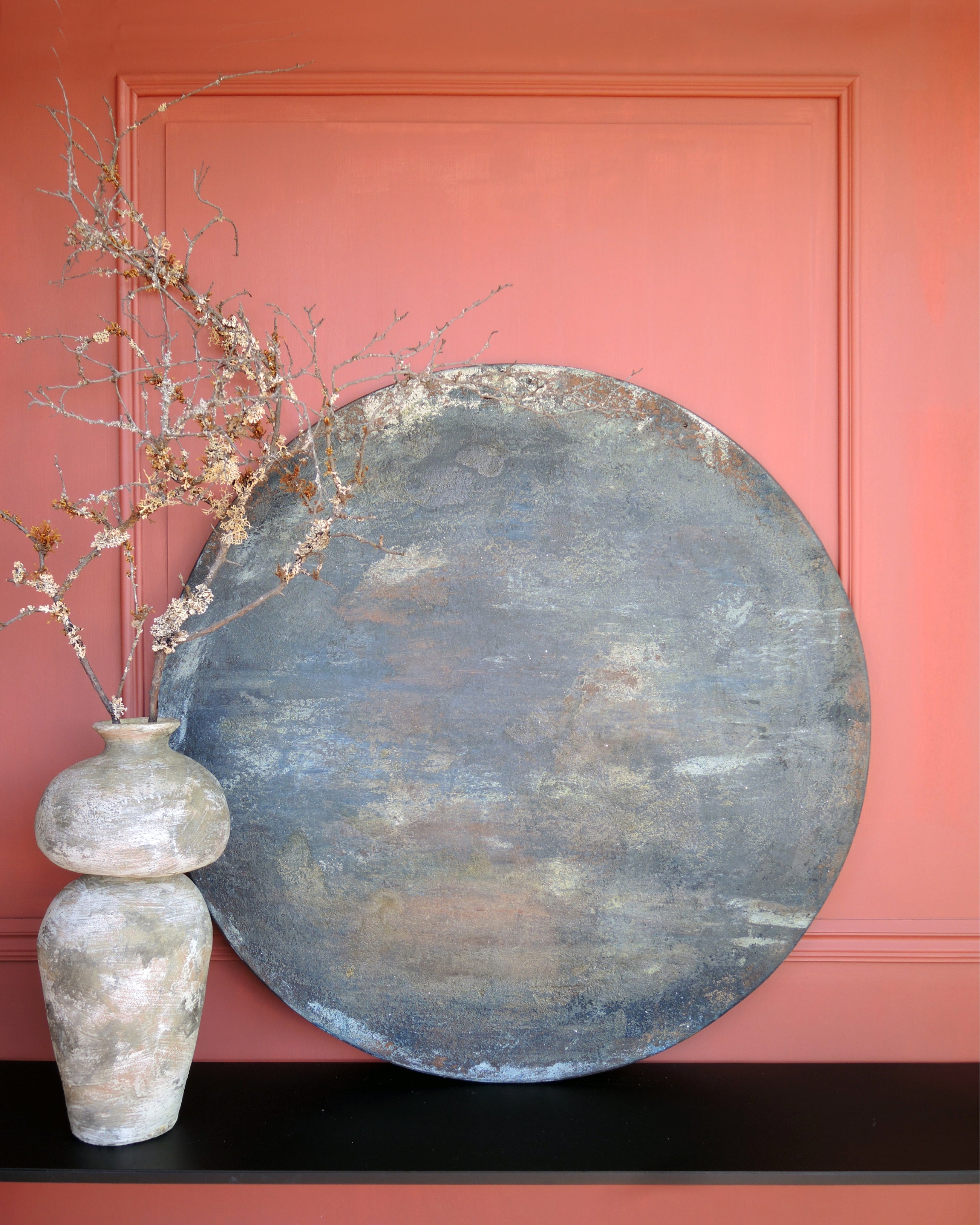 Dark abstract painting on wood shown in a styled interior, layered patina surface with earthy tones