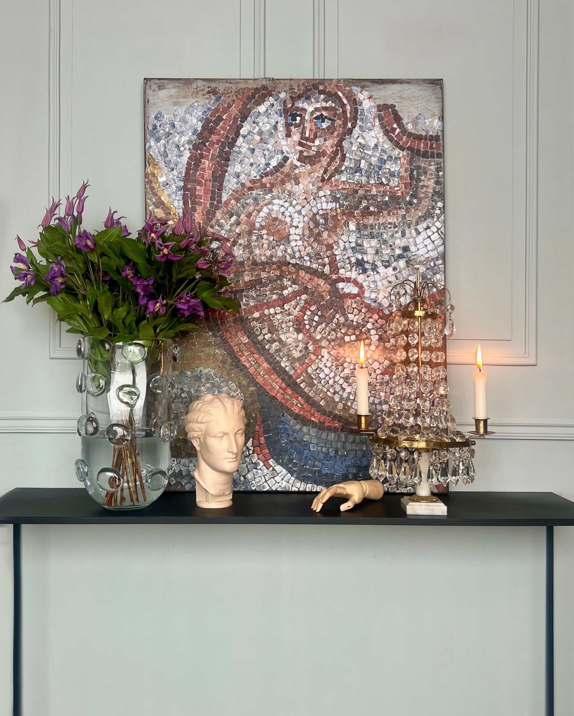 Contemporary mosaic artwork displayed in an elegant interior with classical objects and candlelight.