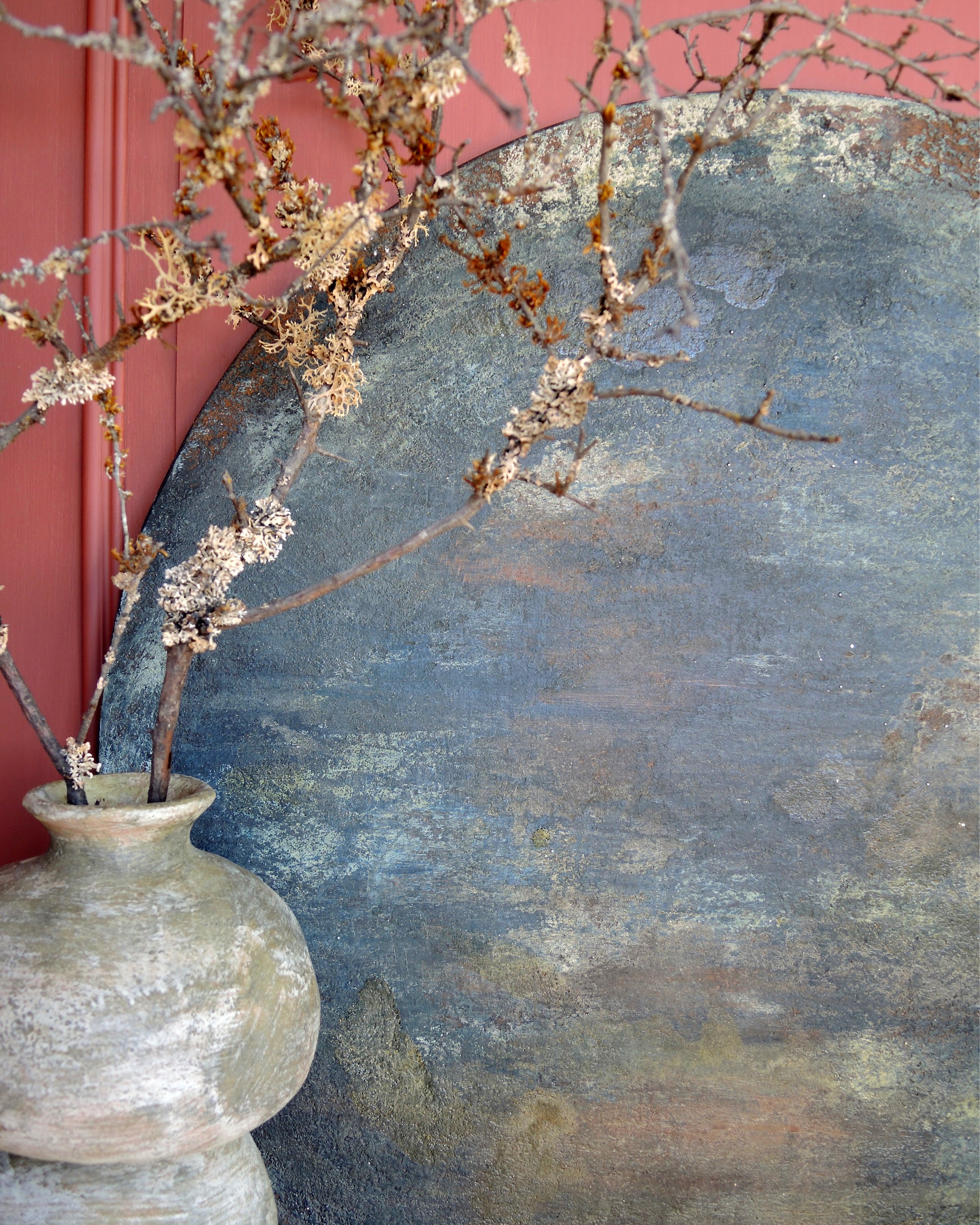 Round abstract painting with textured dark patina surface, styled with objects and flowers in a calm interior
