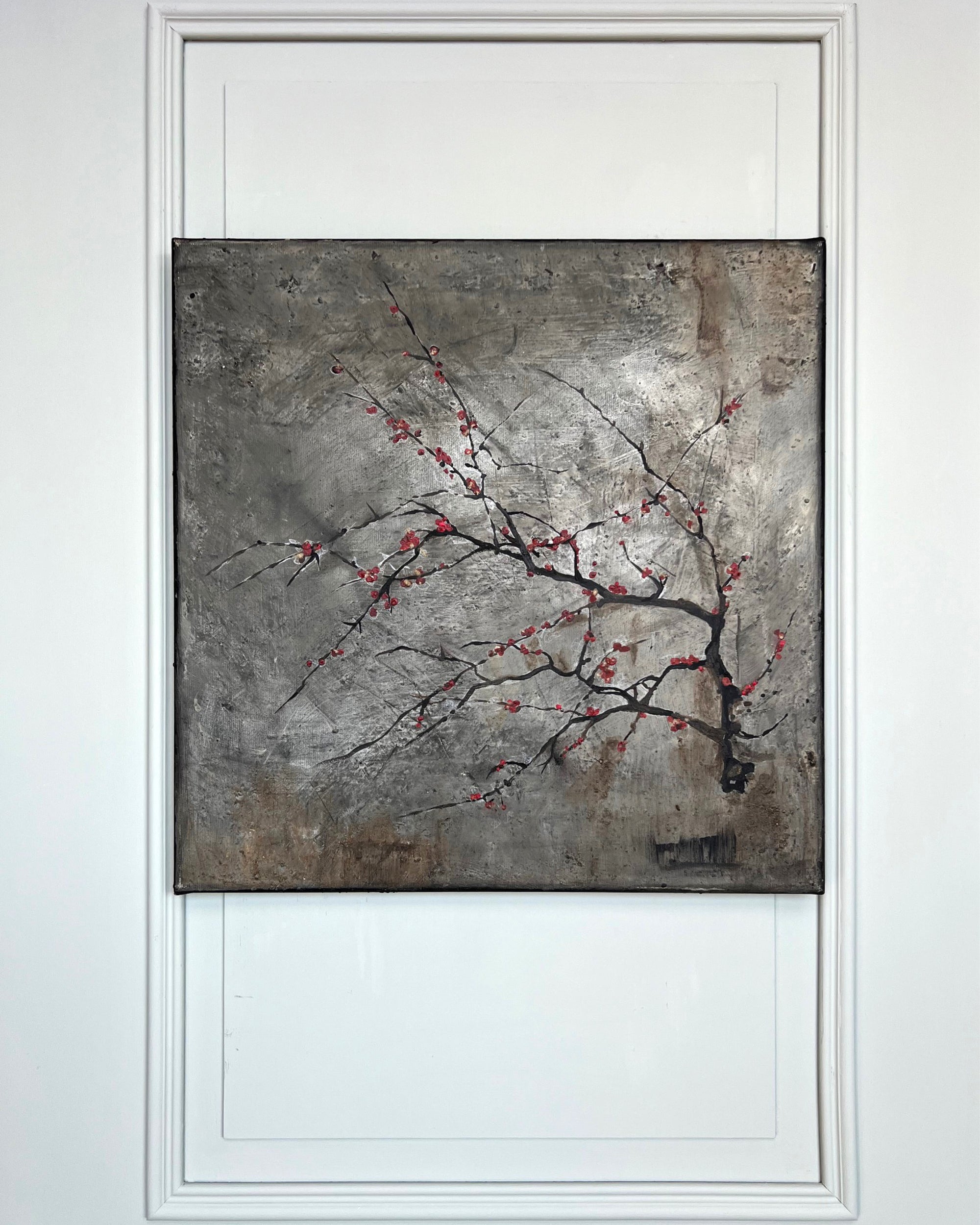 Original square painting displayed on a white wall, featuring a fine branch with red blossoms against a textured grey patina background.