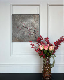 Contemporary square painting with red blossom branch styled in a calm interior setting with sculptural vase and soft natural light.