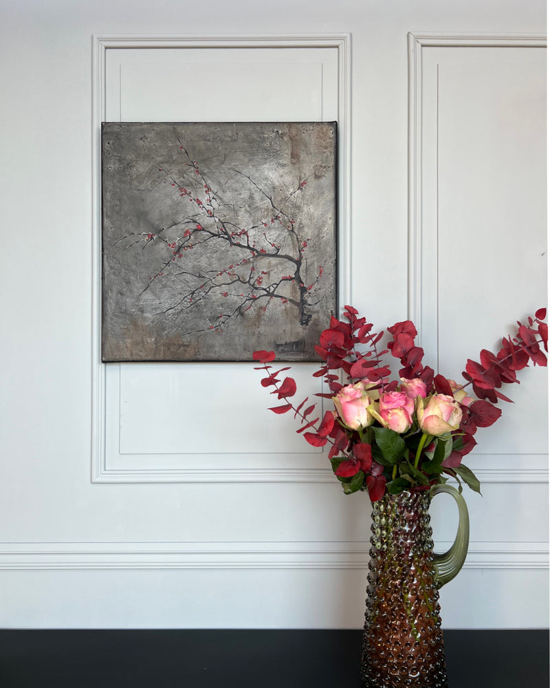 Contemporary square painting with red blossom branch styled in a calm interior setting with sculptural vase and soft natural light.