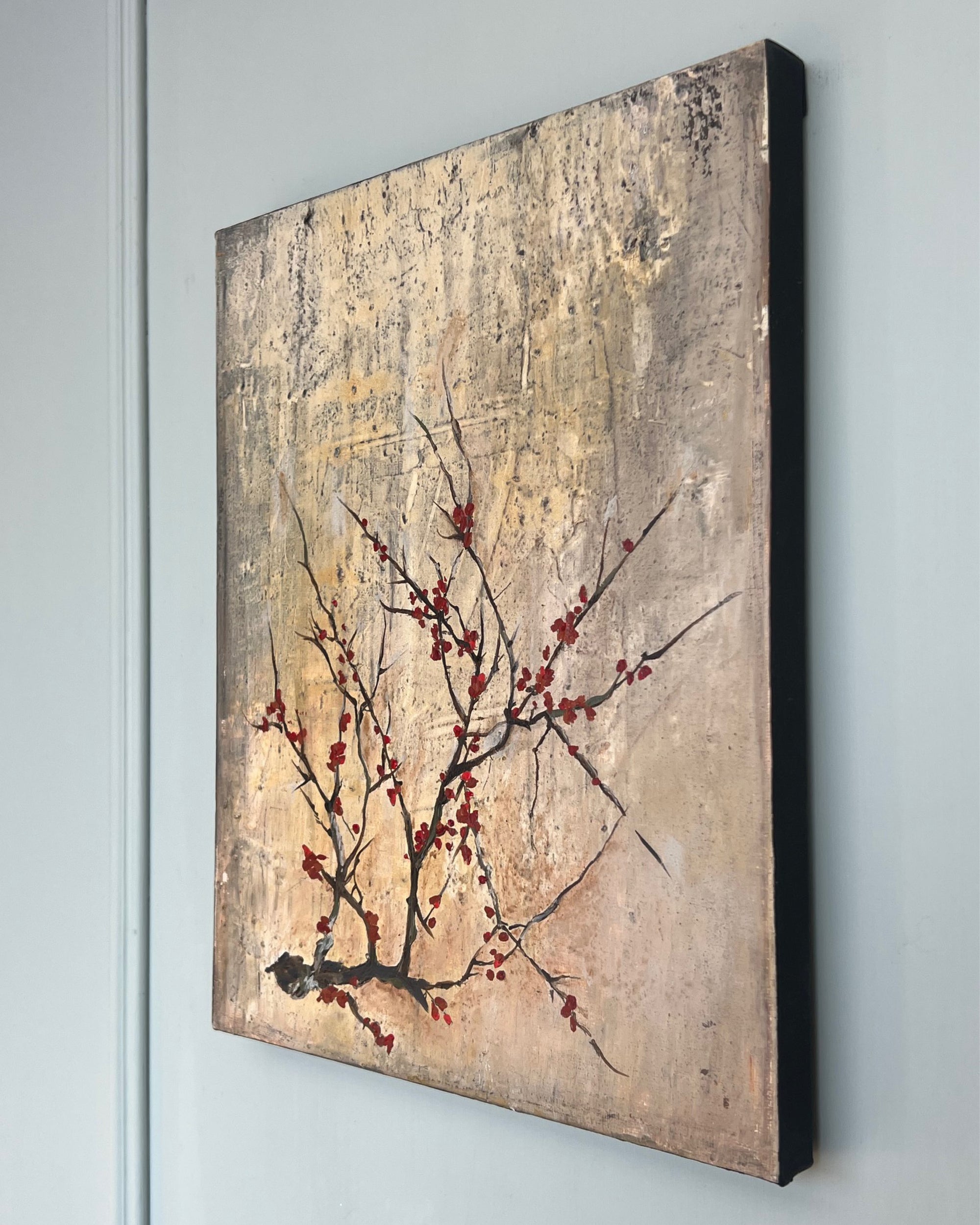 Angled view of a square contemporary painting with visible canvas depth and a restrained branch motif on a weathered grey surface.