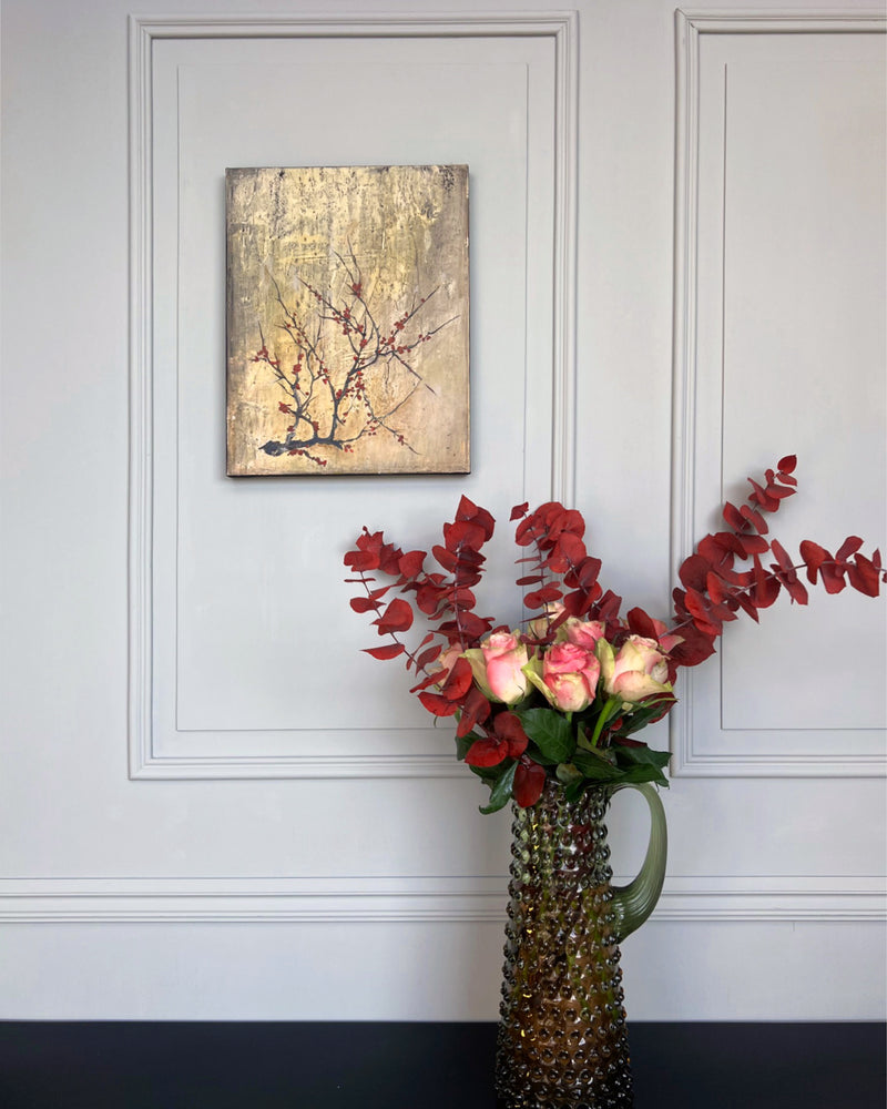 Contemporary square painting with red blossom branch styled in a calm interior setting with sculptural vase and soft natural light.