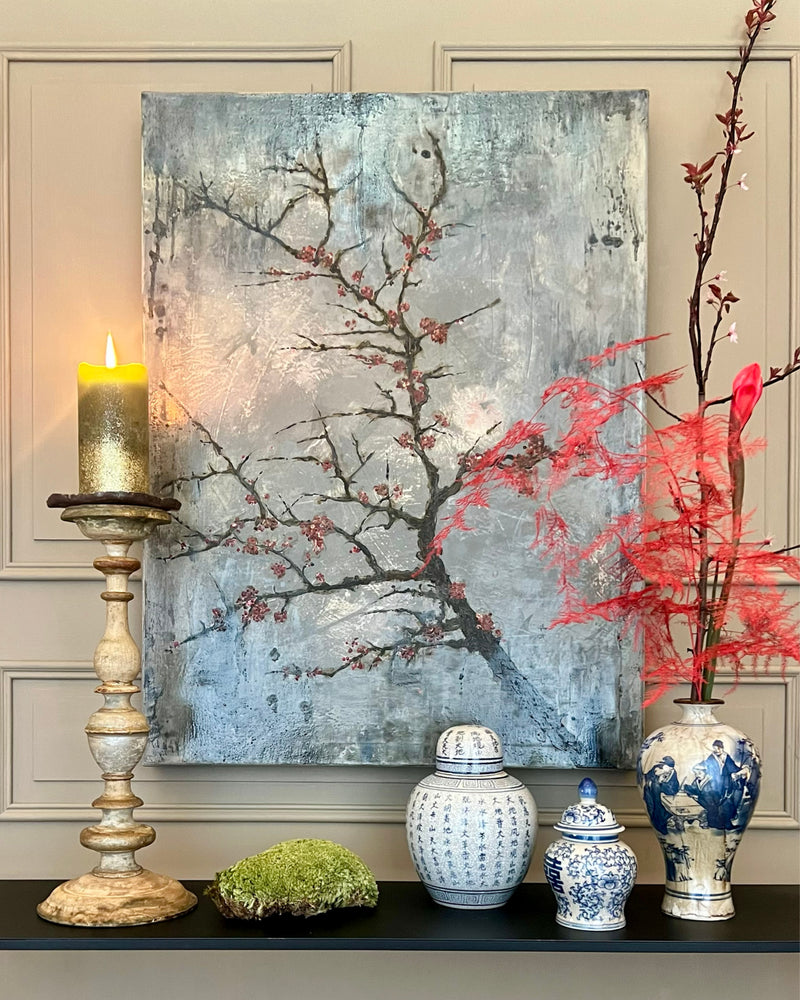 Wabi Sabi original painting displayed in a calm interior setting with candle and ceramic vases, textured grey artwork with red blossom branches.